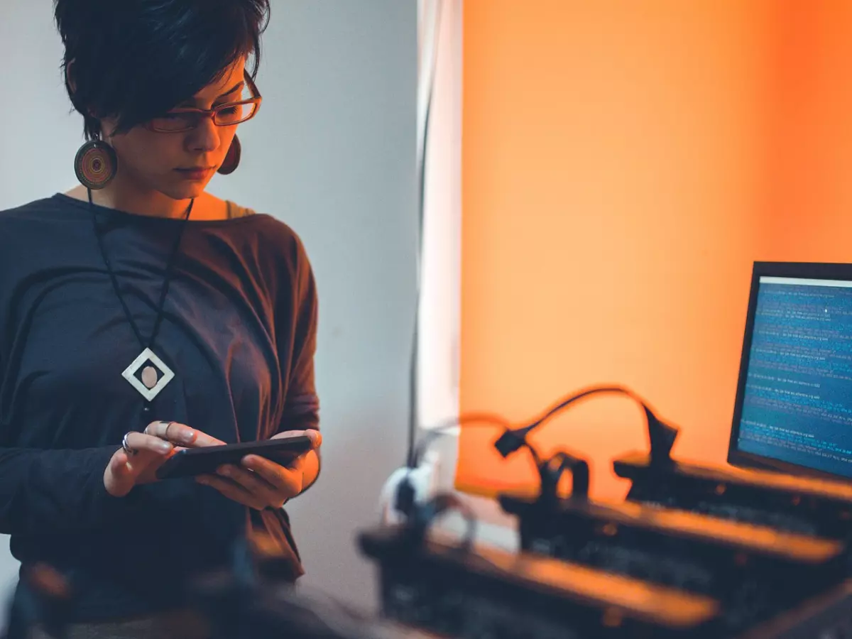 A person is standing in front of a row of bitcoin mining rigs. The person is looking down at their phone. 